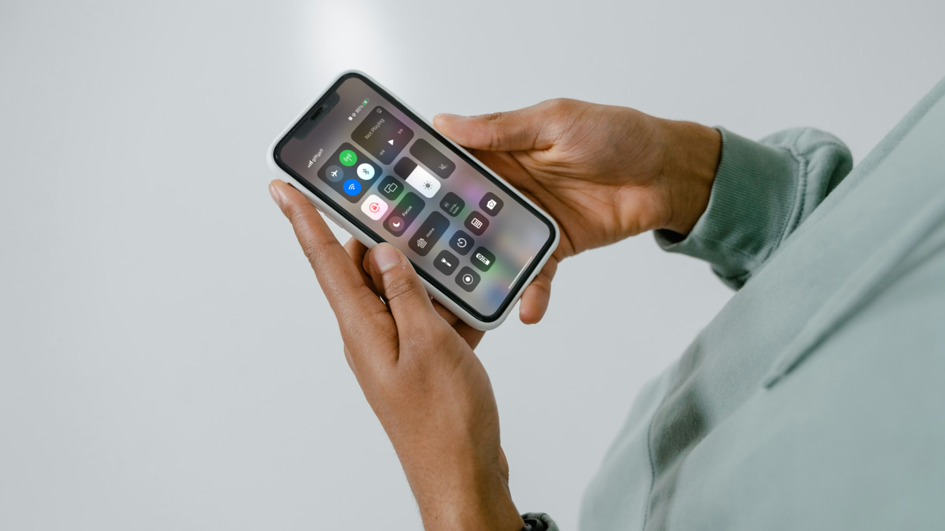 A mockup of an iPhone screen's Control Centre on an iPhone held by a person.