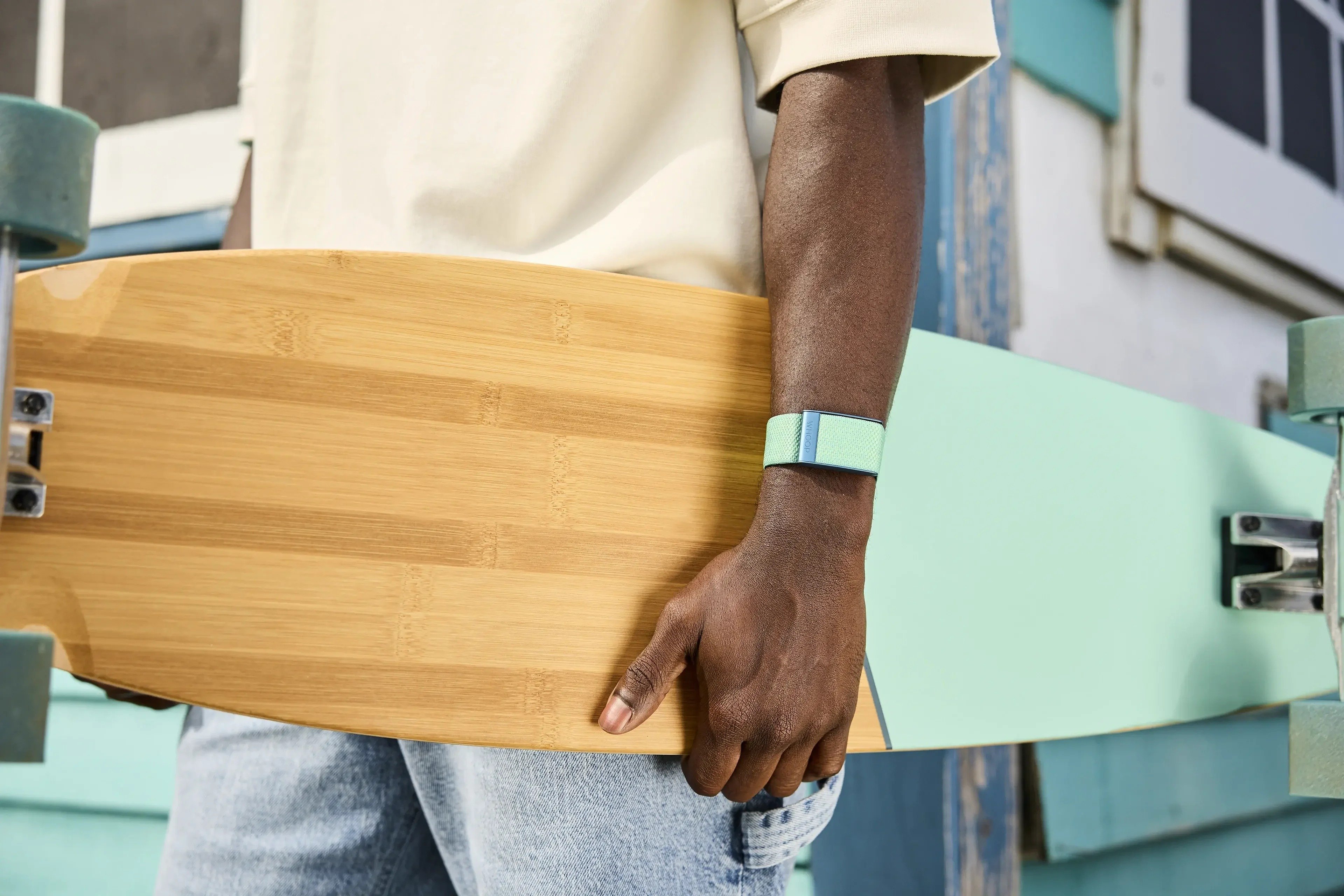 a person wears a light turquoise whoop band on their wrist while holding a wooden longboard that matched the color of the whoop band