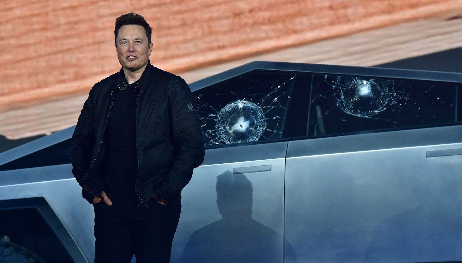 Elon Musk standing in front of a Cybertruck with two bullet marks in its windows.