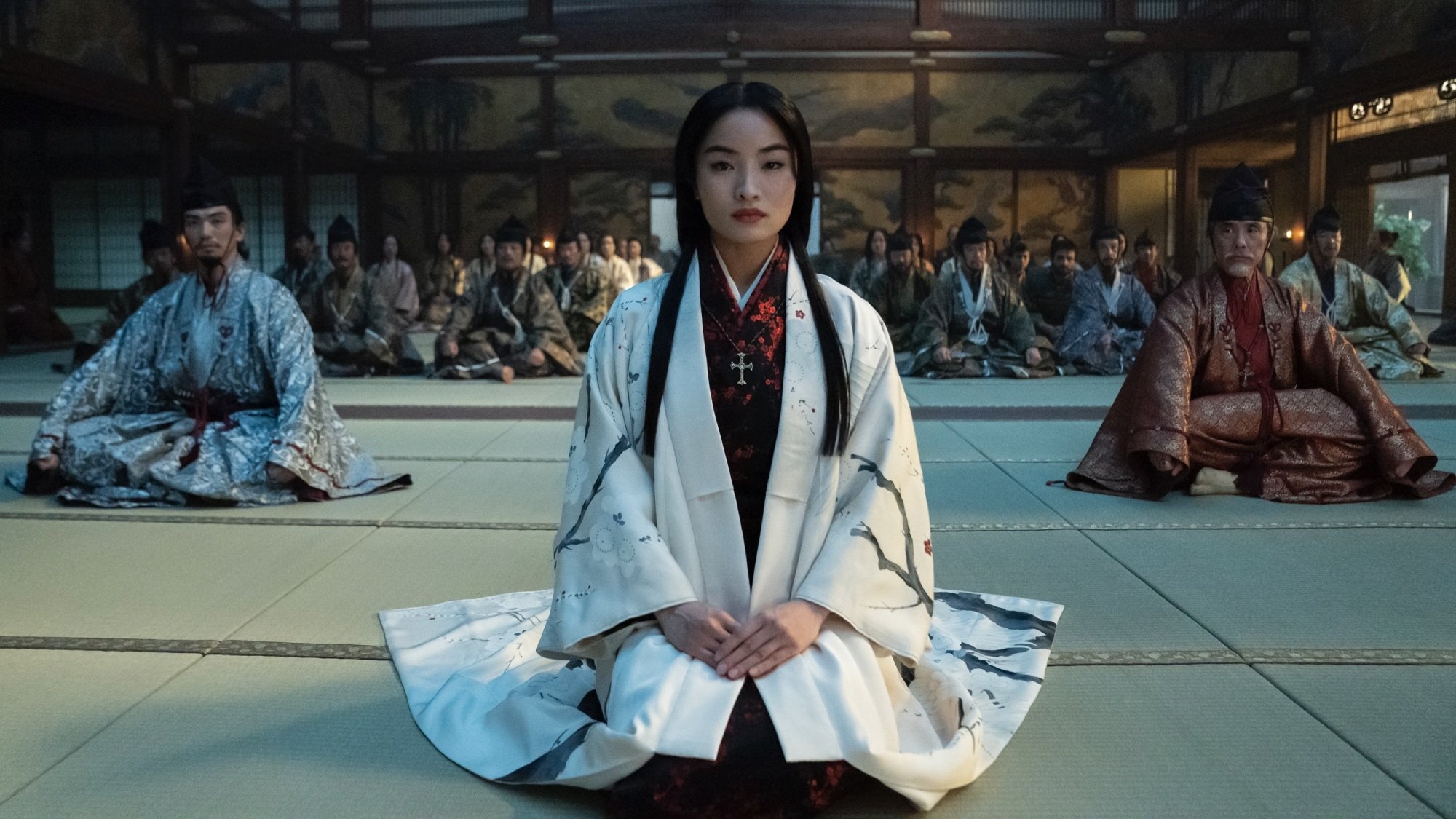 Mariko from "Shōgun" kneels in a crowded hall in a white kosode.