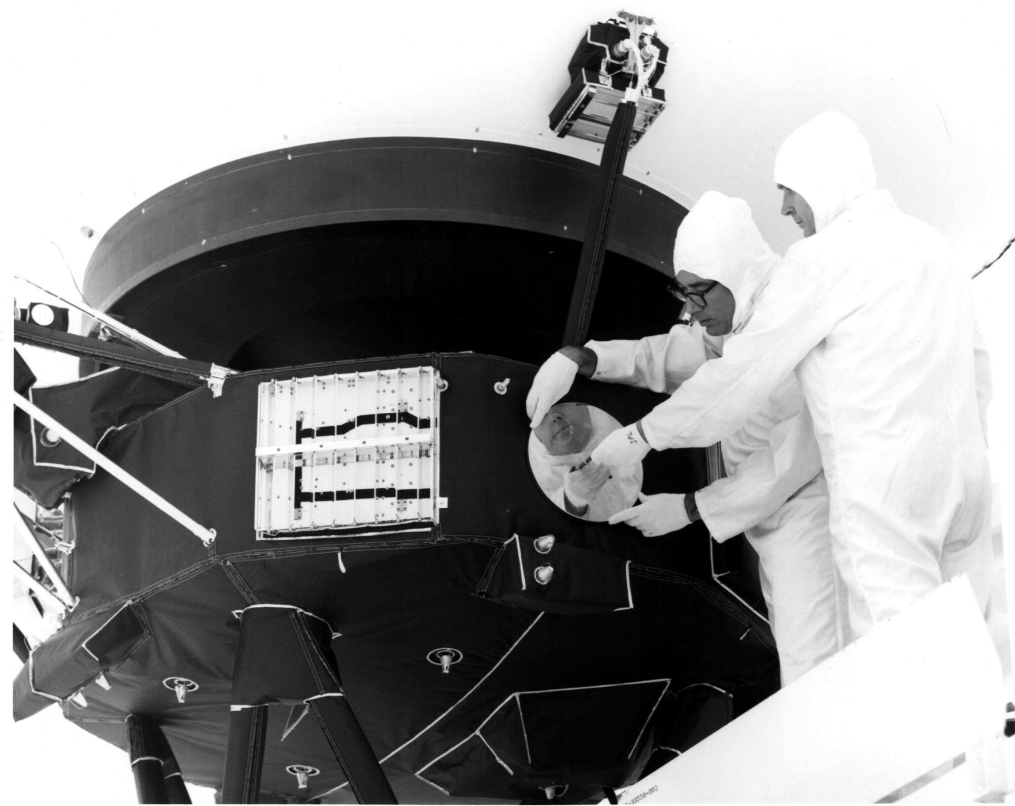 Engineers installing a golden record — containing music, sounds, and imagery from Earth — to the side of Voyager 1. 