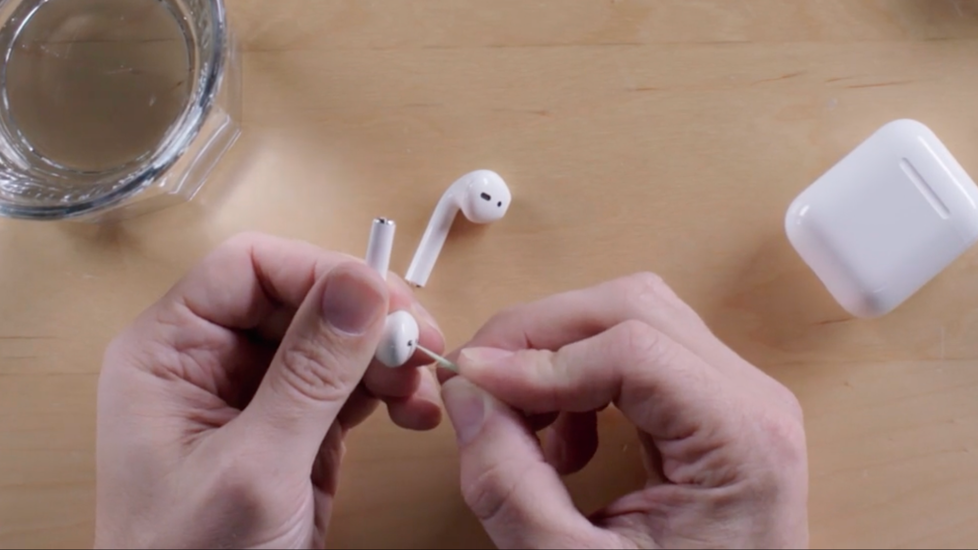 Two white hands, one holding the airpod, the other cleaning it with a toothpick.