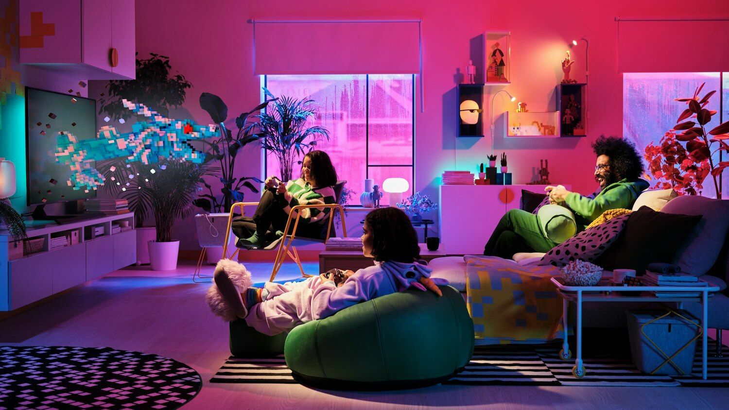Three people sit in a living room lit with pink, purple, and blue tones. A blue pixelated dragon pops out of the TV they are all looking at.